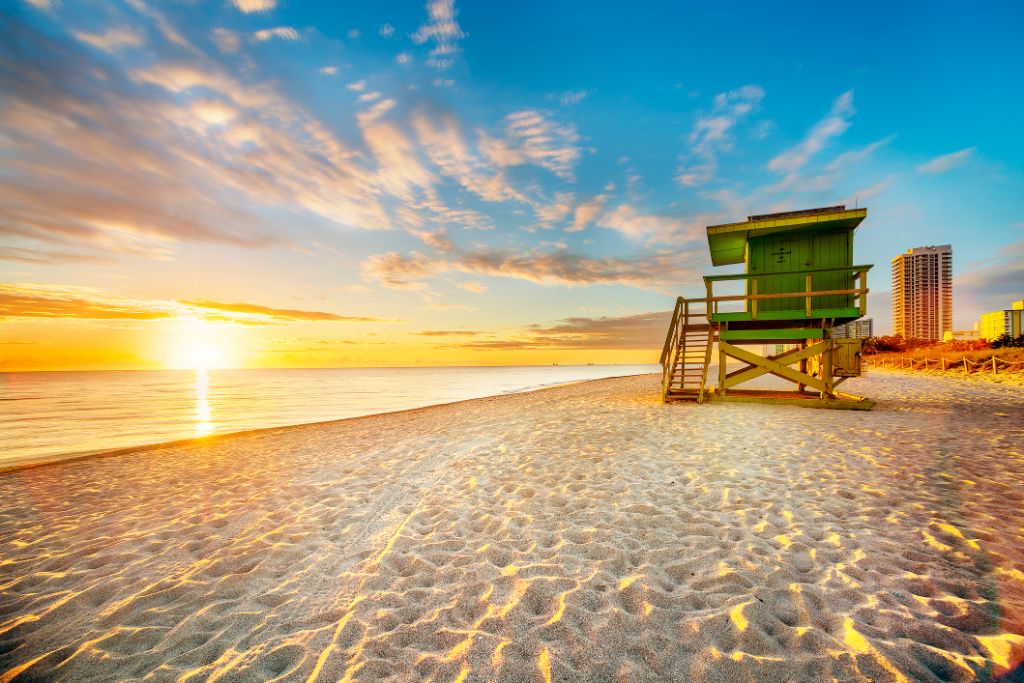 Miami South Beach sunrise with lifeguard tower and coastline with colorful cloud and blue sky.