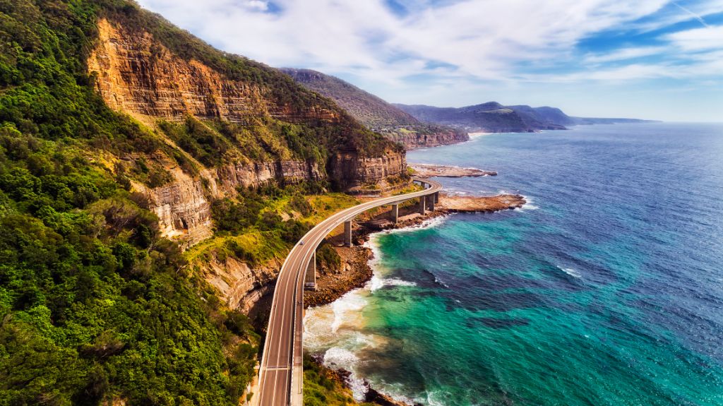 Sea cliff bridge at the edge of steep sandstone cliff on the Grand Pacific drive along pacific coast of Australia, NSW. Aerial view towards distant hill ranges on sunny summer day.