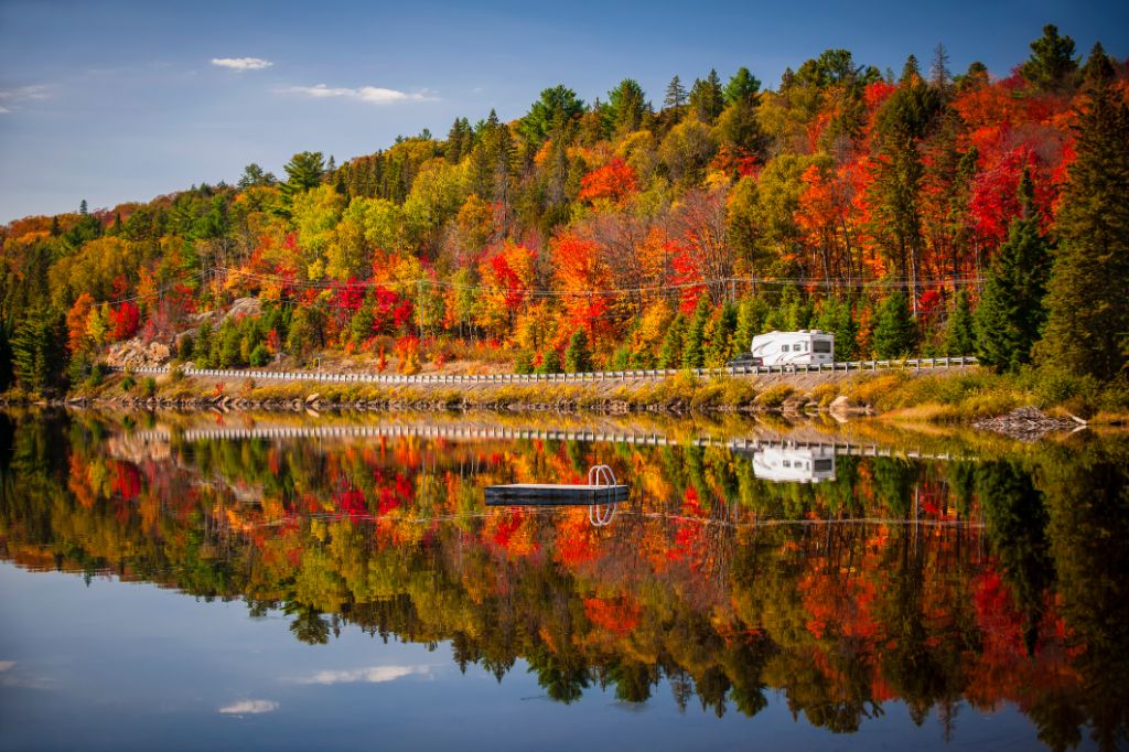 Fall forest with colorful autumn leaves and highway 60 reflecting in Lake of Two Rivers.  Algonquin Park, Ontario, Canada.